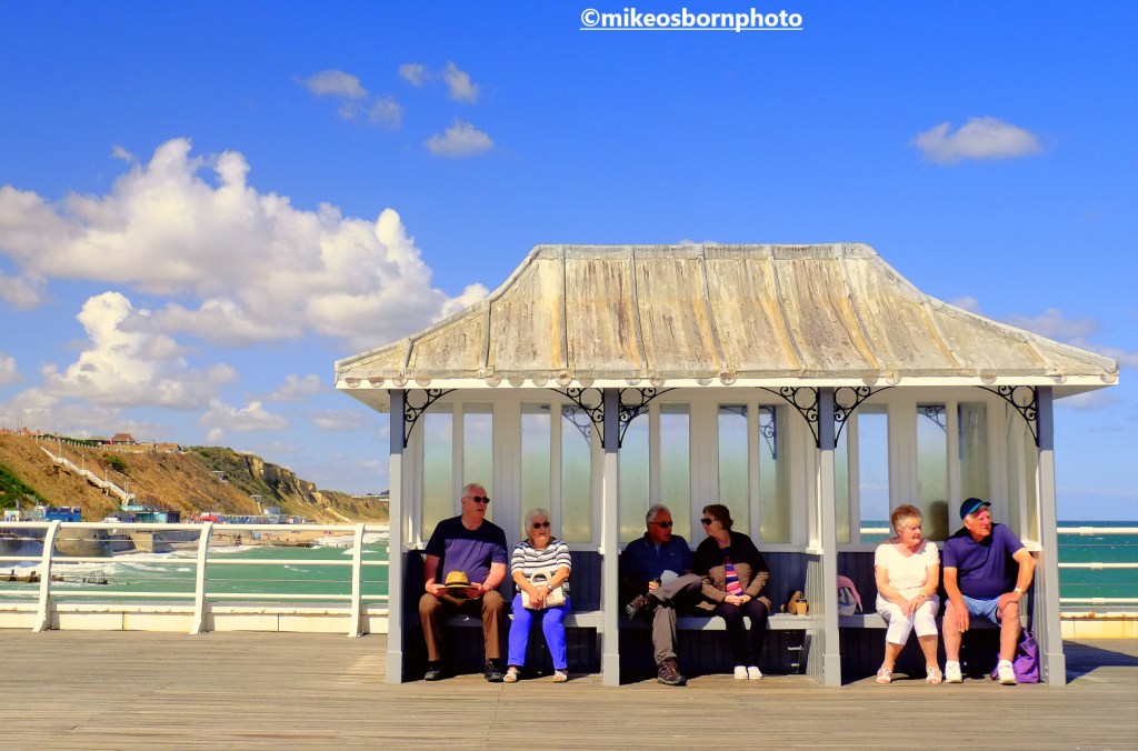 Three couples sit in a shelter on Cromer pier, Norfolk, UK