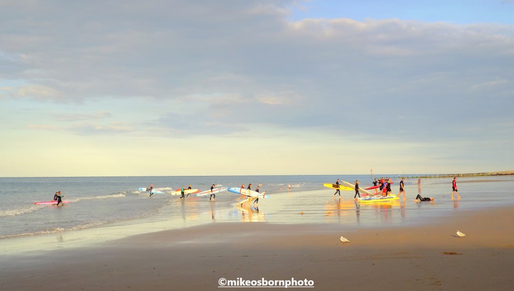 Swimmers with their yellow surfboards running out of the sea on Cromer beach
