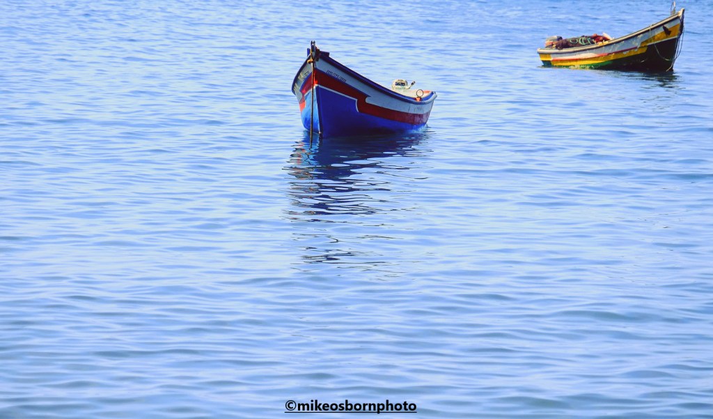 Two colourful Cape Verde fishing boats bob around in the waters off Cidade Velha