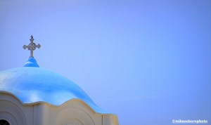 A blue Greek Orthodox church dome against a clear azure sky