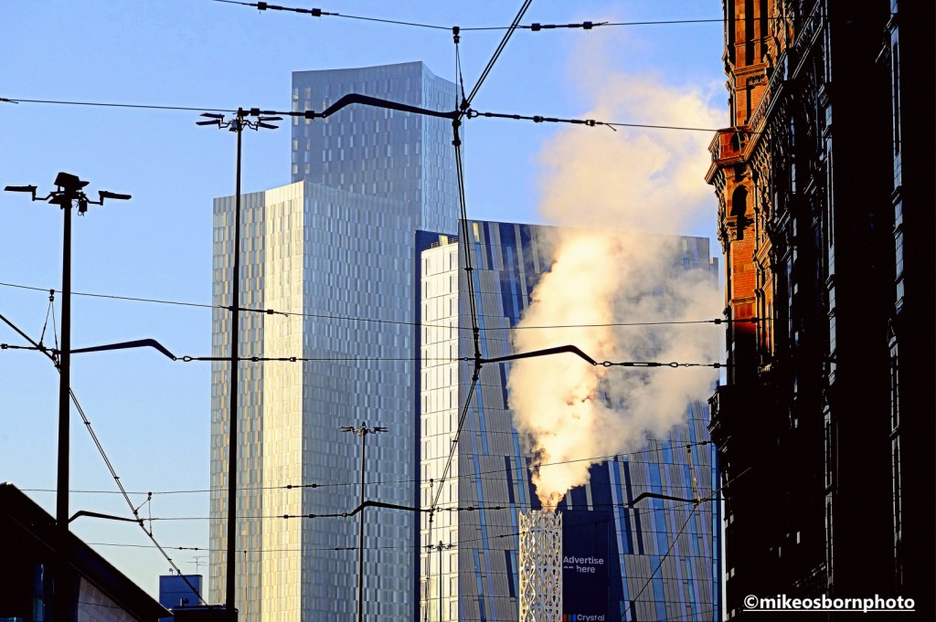 A steam plume in freezing weather among the tall buildings of Manchester.