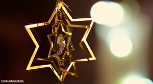 A gold foil Christmas decoration shaped like a star against whie lights.