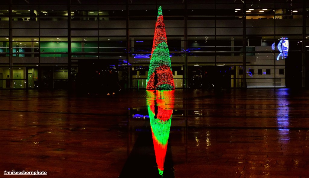 An illuminated Christmas tree reflected in wet weather.