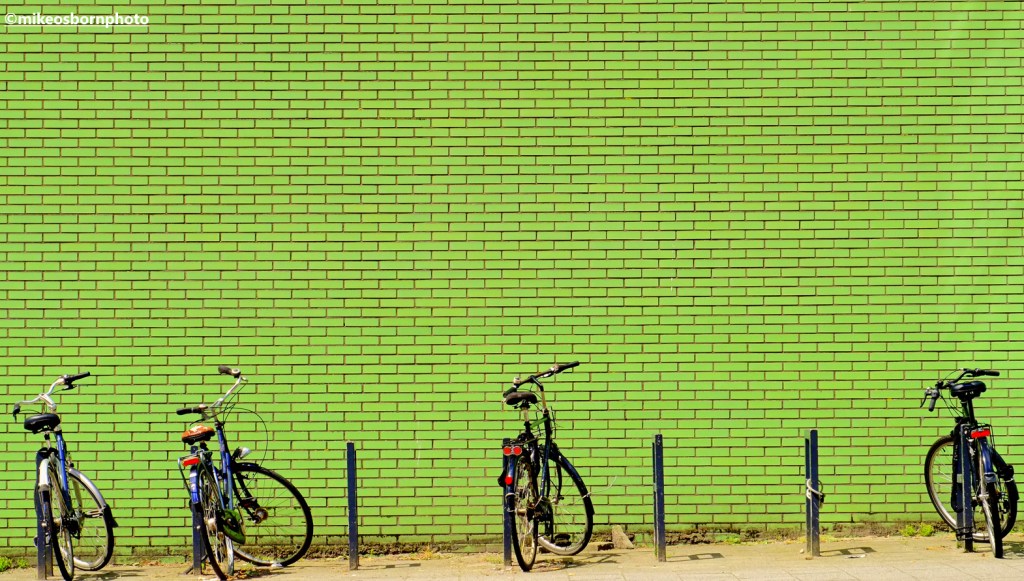 Bicycles in Rotterdam parked next to a green brick wall.