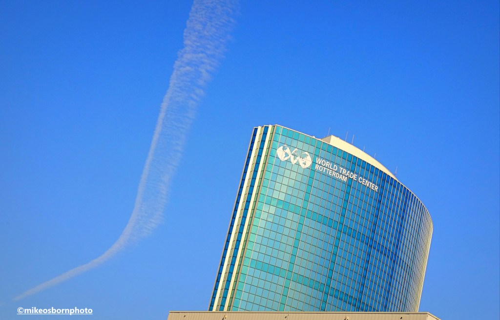 The curved blue glass of Rotterdam's World Trade Center building catches the bright light.