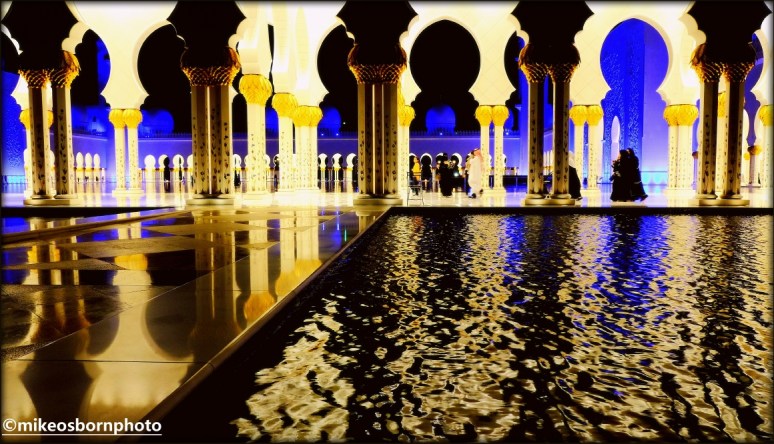 Water and illuminated marble of Sheikh Zayed mosque in Abu Dhabi, seen at night.